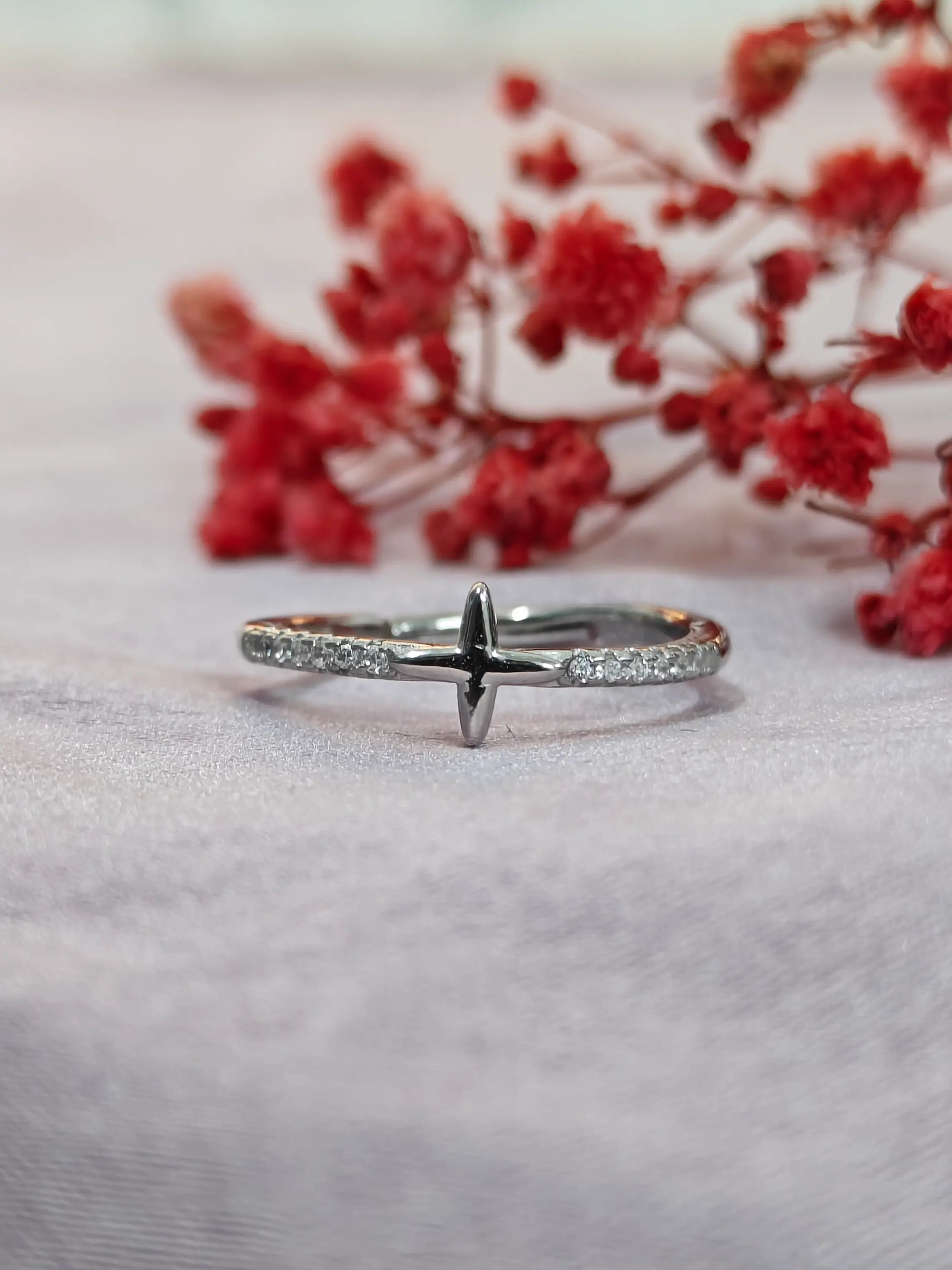 Silver ring with small diamonds on a light gray surface with red flowers in the background